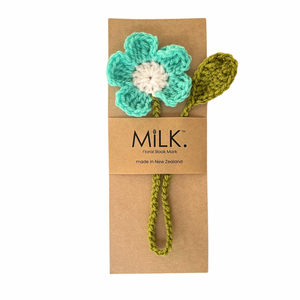 A handmade crochet floral book mark featuring a turquoise and white flower with an olive green loop handle, presented on a brown kraft paper card branded 'MILK. Floral Book Mark'.