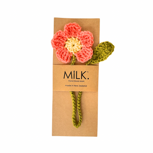 A handmade crocheted flower bookmark with a coral-pink and yellow flower, green stem, and leaf, attached to a brown kraft paper card printed with the brand name 'Milk Book Mark'.