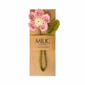 A handmade crochet flower bookmark by the brand MILK. The flower has pink and cream petals with an olive green stem and leaf, attached to a brown kraft paper card that reads 'MILK.