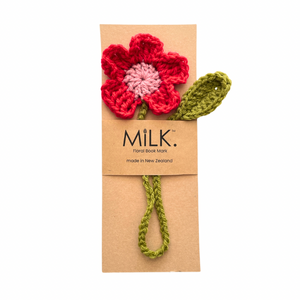 A handmade crochet floral book mark featuring a red and pink flower with an olive green stem and leaf, attached to a brown kraft paper card printed with the brand name 'MILK'.