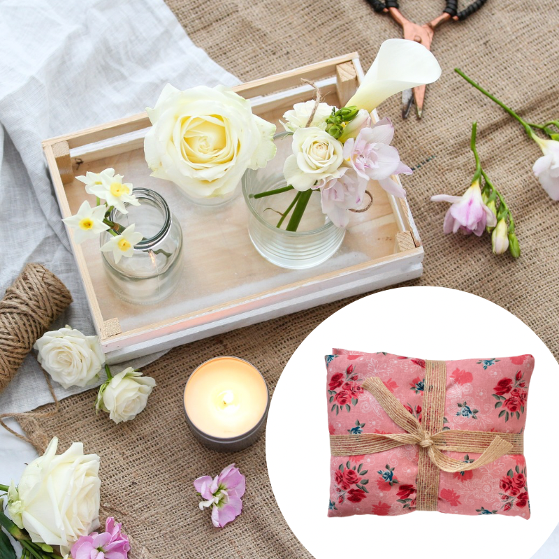Decorative setting with flowers, candles, and a wheat bag on a textured surface.